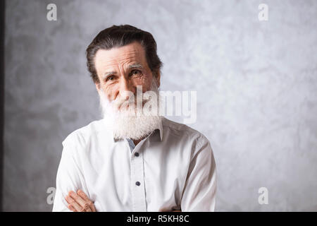 Portrait of contemporary cheerful bearded senior man with wrinkles in white shirt standing on the gray background, modern technology, communication concept Stock Photo