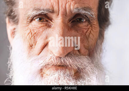 Portrait of contemporary cheerful bearded senior man with wrinkles in white shirt standing on the gray background, modern technology, communication concept Stock Photo