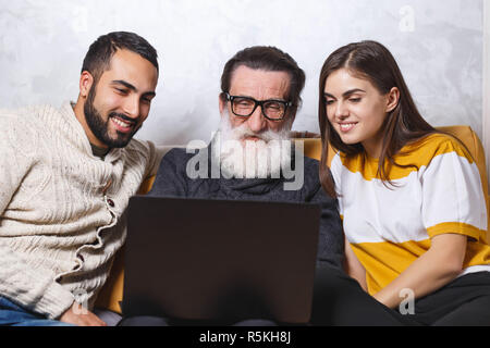 Senior bearded father in glasses sitting with his children on the yellow sofa in the light living room and watching movie, modern technology, communication concept