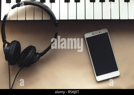 Headphones, synthesizer and a telephone lying on a beige background Stock Photo