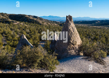 A group of three unusual, cone-shaped rock formations in Kasha-Katuwe Tent Rocks National Monument with distant view of valley and mountains Stock Photo