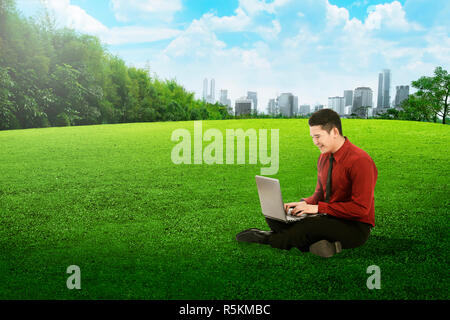 Asian business man working with laptop and sitting on the grass Stock Photo