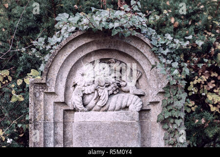 Old tombstone on german cemetery in Berlin Tegel showing birds, a dove and flowers sculptured in stone Stock Photo