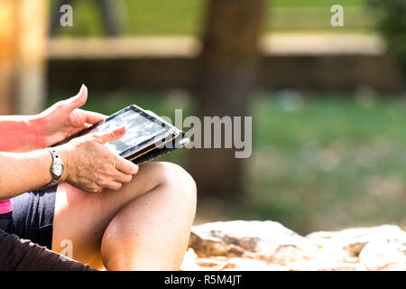 A mature female hands using a tablet sitting in a park outdoors. Stock Photo