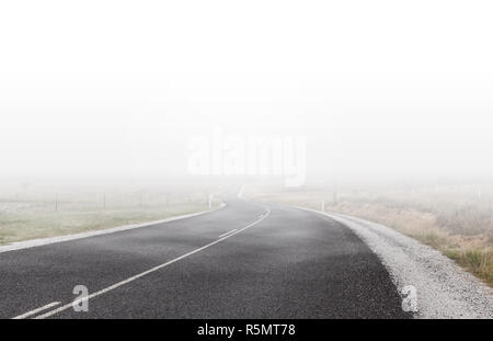 Winding rural road disappearing in the distance under low clouds and fog Stock Photo