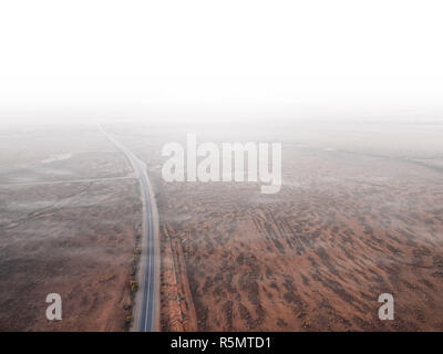 Aerial view of road passing through red desert land and disappearing in white fog Stock Photo