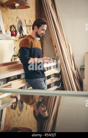 Young craftsman using phone in his workshop Stock Photo