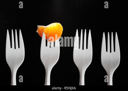 Four white plastic forks on dark. One fork with tangerine segment Stock Photo