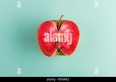Sliced in half apple fruit with vivid red flesh isolated on cyan background, placed in center Stock Photo