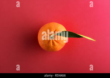Whole ripe mandarin with one green leaf, viewed from above on in center, isolated on red background Stock Photo