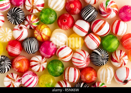 Colorful round candies of red, white, green, yellow and black colors with stripes, sitting on table surface in one layer, top view in full frame Stock Photo