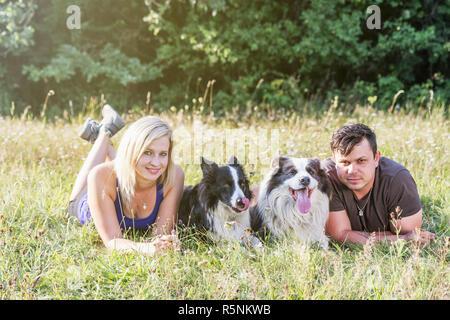 Young man and woman are lying in grass with a pair of dogs Stock Photo