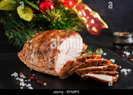 Roasted sliced Christmas ham of turkey on dark rustic background. Festival food. Stock Photo