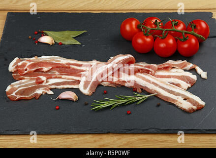 Raw bacon slices, spice and tomato on black board Stock Photo