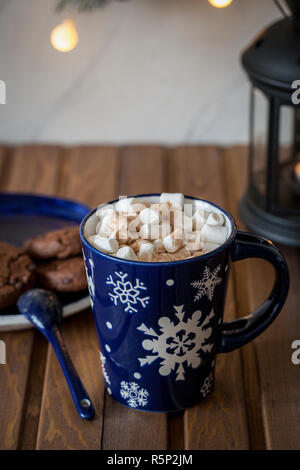 Sweet tasty hot chocolate with marshmallows in blue cup with spoon, lantern with candle and plate with cookies at wood background. Christmas compositi Stock Photo