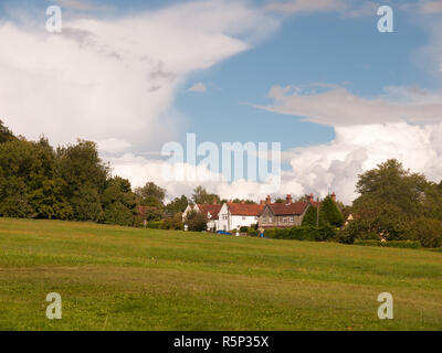 interesting sloped green lawn with country houses in background and blue and white cloud sky Stock Photo