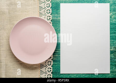Empty plate on wooden tabletop with tablecloth and blank paper. Flat lay. Stock Photo
