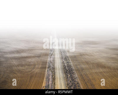 Aerial view of dirt road between plowed fields vanishing in low clouds and fog Stock Photo