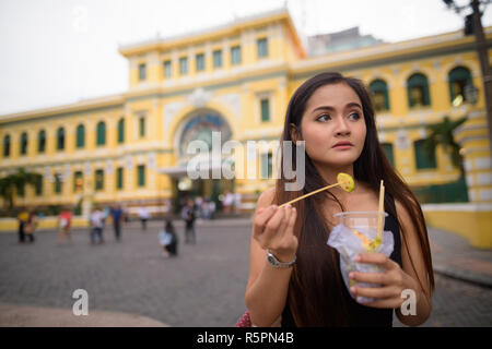 Asian woman eating in front of Saigon Central Post Office Stock Photo