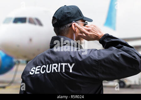 Security Guard Listening To Earpiece Against Building Stock Photo