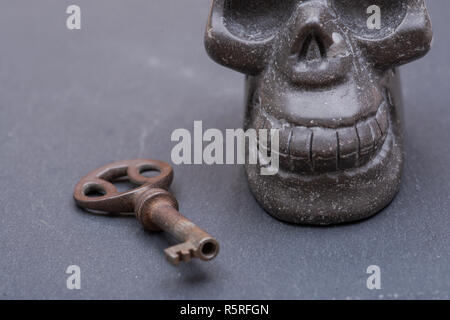 Old antique vintage metallic key and stone carved skull on natural stone background. Stock Photo