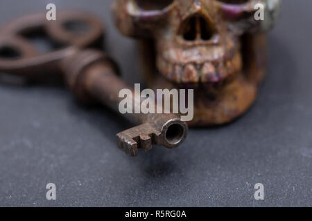 Old antique vintage metallic key and stone carved skull on natural stone background. Stock Photo