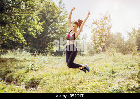 Young happy sport woman jumping high outdoor on meadow. Toned image. Stock Photo