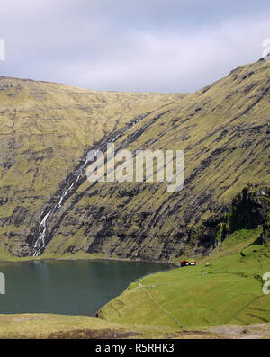 Waterfall at Saksun with tiny red tin roof house on the side of the sea inlet in the Faroe Islands Stock Photo