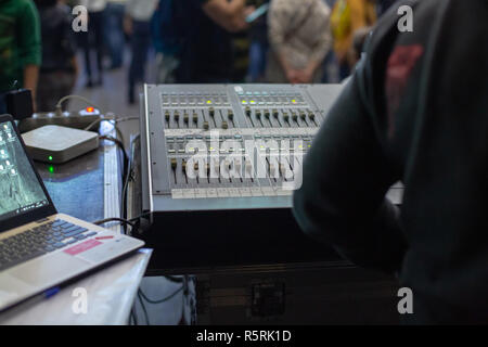Soundman working on the mixing console behind the concert crowd. View from the back. Stock Photo