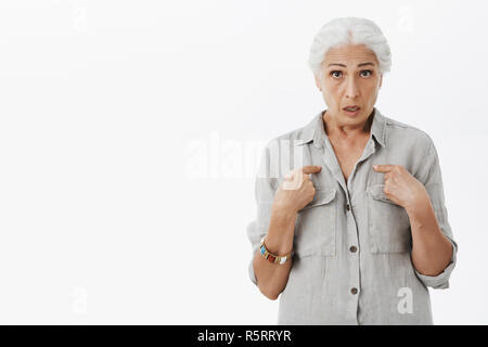 Waist-up shot of confused and stunned senior woman feeling questioned and frustrated pointing at herself staring concerned at camera trying understand Stock Photo