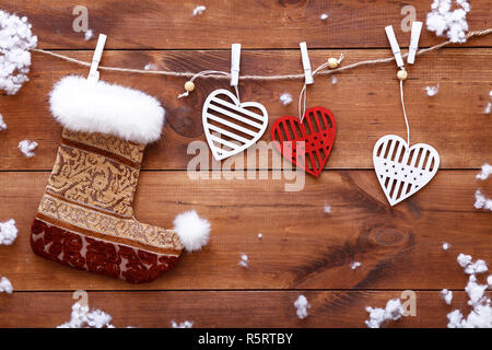 Christmas stocking sock and white red hearts hanging on brown wooden background with snow, holiday decorations for New year Valentines Day celebration Stock Photo