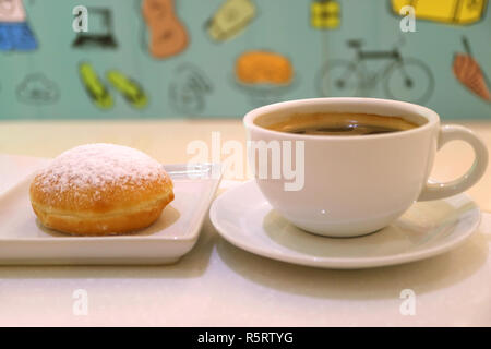 Cup of hot coffee and a strawberry jam filled doughnut with blurred colorful wall paper in background Stock Photo