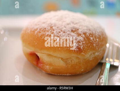 Closed up a strawberry jam filled doughnut served on white plate with fork Stock Photo