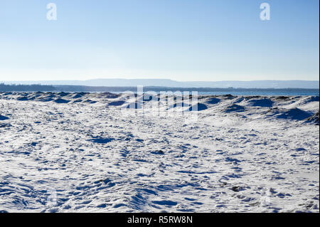 Frozen ice, snow, and sand dunes on beach with hills in distance. Stock Photo