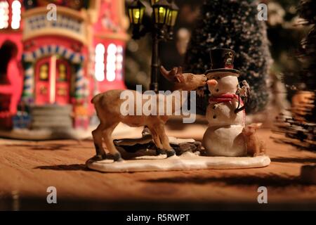 Festive Christmas scene of a toy figurine reindeer biting the carrot nose of a snowman. From an electric train set scene. Stock Photo