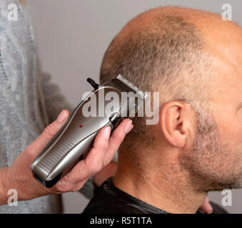 Portable electric hair clippers being used to give a balding man a crew cut hair style. Stock Photo