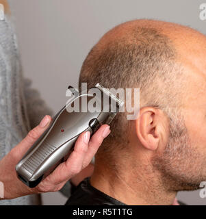 Portable electric hair clippers being used to give a balding man a crew cut hair style. Stock Photo