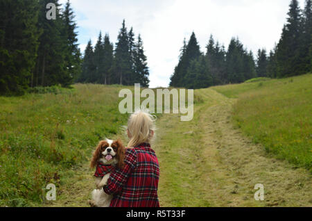 Woman dressed in royal stewart hiking with her dog - Cavalier King Charles Spaniel - having a collar with a same pattern on mountain path Stock Photo