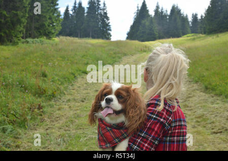 Woman dressed in royal stewart hiking with her dog - Cavalier King Charles Spaniel - having a collar with a same pattern hiking on mountain path Stock Photo