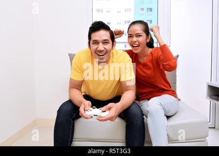 Happy asian couple sitting on couch and playing video games Stock Photo