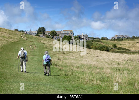 Elderly couple with backpacks walking towards the picturesque village of Worth Matravers on the Isle of Purbeck, Dorset, England, UK