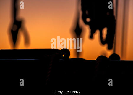 Ropes, nets, cables, pulleys and bollards as shadows against a colorful sky of red and blue colors of the sunset. Hitorical details of an old ship in  Stock Photo