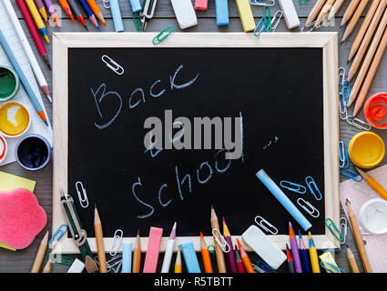 Back to school inscription written on chalkboard with kids supplies for modern primary education, color pencils, paints and other multicolored accesso Stock Photo