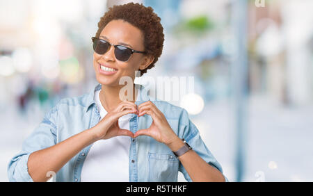 Beautiful young african american woman wearing sunglasses over isolated background smiling in love showing heart symbol and shape with hands. Romantic Stock Photo