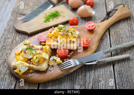 Hearty scrambled eggs with bacon cubes and chives served hot on toasts Stock Photo