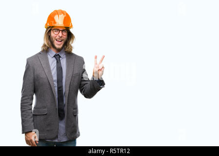 Young handsome architec man with long hair wearing safety helmet over isolated background smiling with happy face winking at the camera doing victory  Stock Photo
