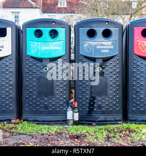Two empty wine bottles stood in front of recycling bins Stock Photo