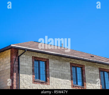 The house is made of beige bricks, the roof is covered with bitumen shingles. Metal plastic windows on the house. Stock Photo