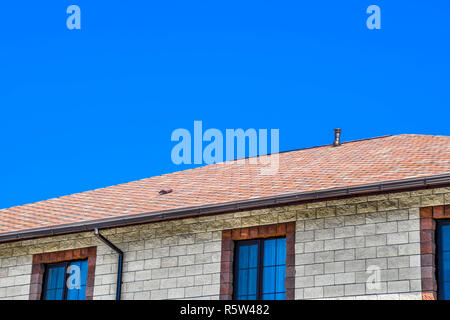 The house is made of beige bricks, the roof is covered with bitumen shingles. Metal plastic windows on the house. Stock Photo