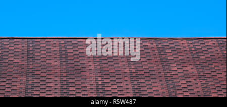 Roof from multi-colored bituminous shingles. Patterned bitumen shingles. Bituminous burgundy roof. Stock Photo